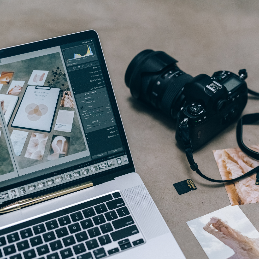 Laptop exibindo software de edição de imagem ao lado de uma câmera DSLR e cartões de memória, representando a criação e edição de conteúdo visual.