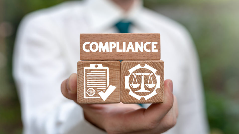 Blocos de madeira com ícones de compliance, representando a importância da conformidade legal e ética nos negócios.