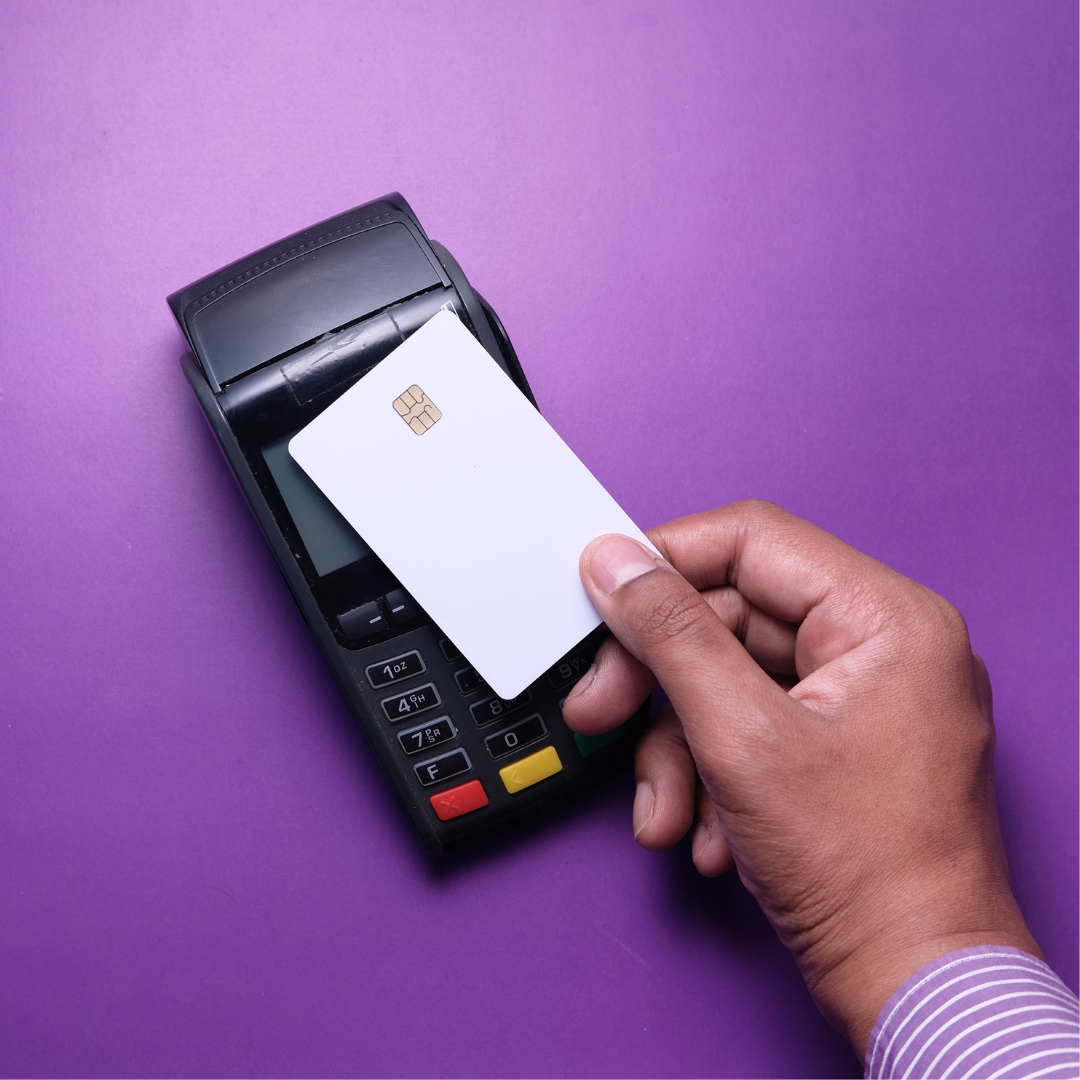 Mão segurando um cartão em uma máquina de pagamento digital em fundo roxo.